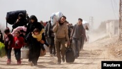 La gente carga sus pertenencias mientras huyen del enclave rebelde de Hammouriyeh, en el pueblo de Beit Sawa, Ghouta oriental, Siria, el jueves, 15 de marzo de 2018.