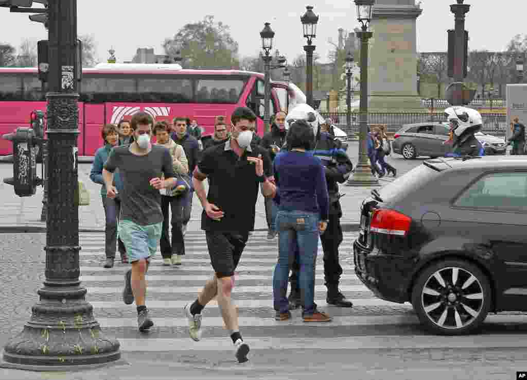 Two joggers wearing protective masks run past a police officer at Concorde Square in Paris, March 17, 2014.