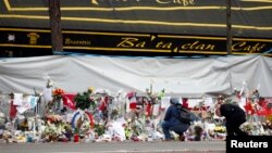 FILE - People mourn in front of the screened-off facade of the Bataclan Cafe adjoining the concert hall, one of the sites of the deadly attacks in Paris, France, a day before a ceremony to pay tribute to the 130 victims, Nov. 26, 2015. 