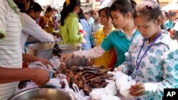កម្មកររោងចក្រកាត់ដេរទិញម្ហូបឆ្អិនស្រាប់ថោកៗសម្រាប់អាហារថ្ងៃត្រង់នៅខាងមុខរោងចក្រនៅក្នុងទីក្រុងភ្នំពេញនៃប្រទេសកម្ពុជា។
