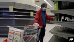Seorang pria yang mengenakan masker dan tas plastik sebagai sarung tangan berjalan melewati rak kosong kertas tisu di sebuah supermarket di Hong Kong, Jumat, 7 Februari 2020. (Foto: AP)