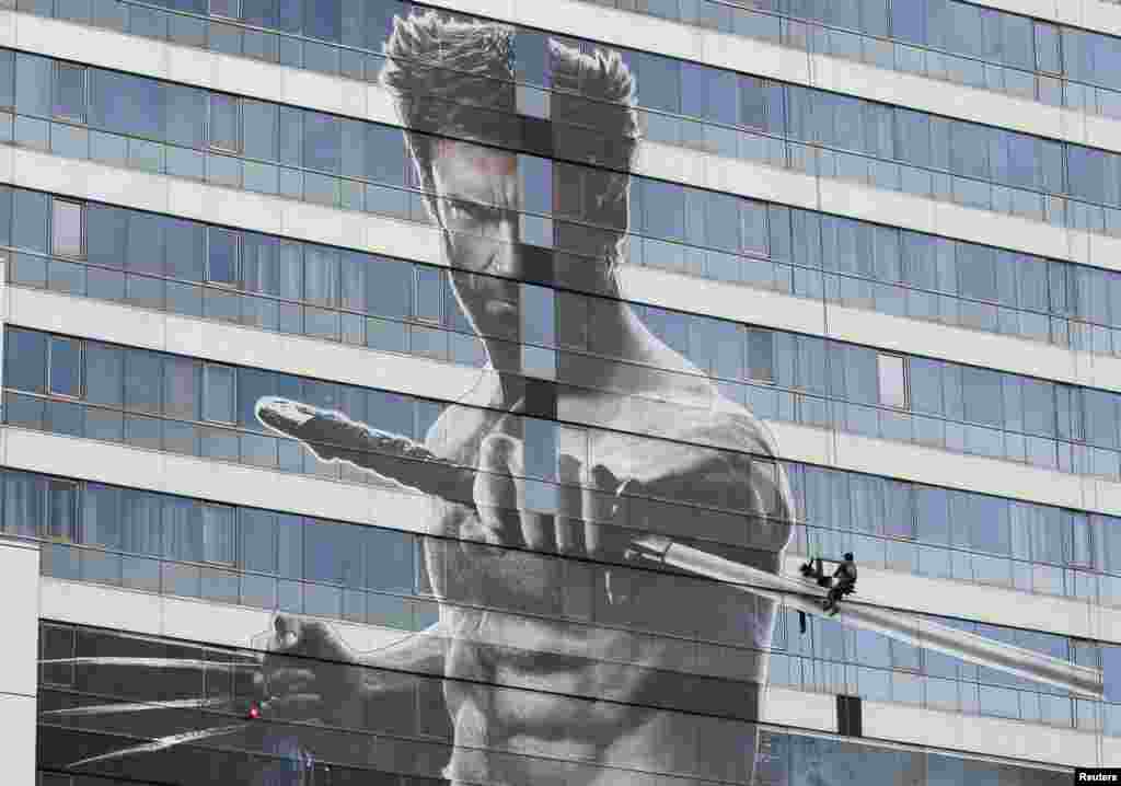 Seorang pekerja memasang sebuah poster raksasa film baru Hugh Jackman berjudul "The Wolverine" di sebuah gedung bertingkat di Bangkok, Thailand.