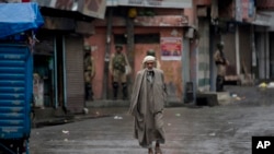 A Kashmiri man walks as Indian paramilitary soldiers stand guard during security lockdown in Srinagar, Indian controlled Kashmir, Wednesday, Aug. 14, 2019.