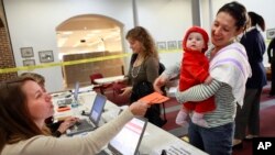 FILE - Election officer Devon Tutak, left, hands a verified voters registration form to Carly von Schaumburg, holding her daughter Alix von Schaumburg, at the polling site at Alexandria City Hall in Alexandria, Va.