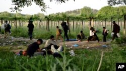 FILE - Afghan migrants rest in the open as others pass by after crossing illegally into Macedonia from Greece, near the town of Gevgelija, Macedonia, May 6, 2015. 