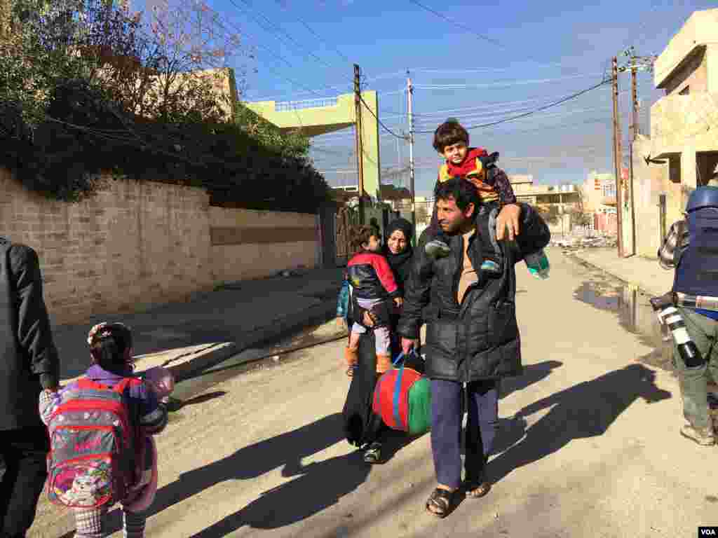 A father carries his child on his shoulders as he flees Mosul with his family, in Mosul, Iraq, Jan. 12, 2017. (K. Omar/VOA Kurdish)