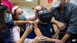 Anak Israel Rafael Peled melihat melalui kacamata realitas virtual VR saat ia menerima vaksin Pfizer-Biontech Covid-19 dari staf medis di Rumah Sakit Sheba Tel Hashomer di Ramat Gan, Israel, Senin, 22 November 2021. (Foto: AP)