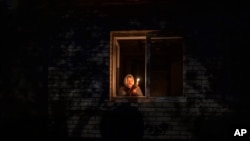 ARCHIVO - Catherine, de 70 años, mira por la ventana mientras sostiene una vela para iluminar el interior de su casa durante un corte de energía, en Borodyanka, región de Kyiv, Ucrania, el jueves 20 de octubre de 2022. (AP)