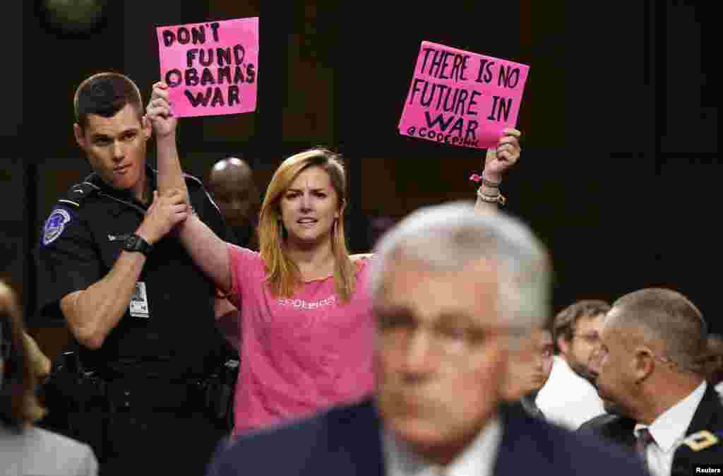 An anti-war protester is escorted out of the Senate Armed Services Committee hearing by a police officer, in Washington, Sept. 16, 2014