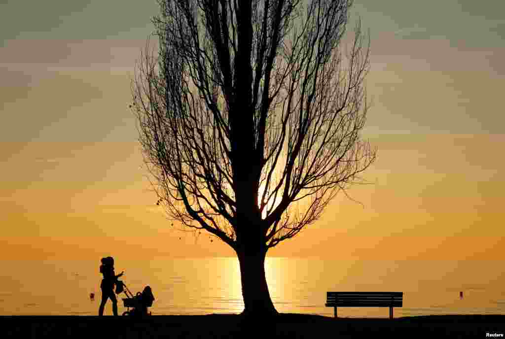 A woman pushes a pram on an autumn evening in a park near Lake Leman in Lutry, Switzerland.