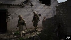 FILE - Ukrainian government soldiers walk past a destroyed home near the line separating Ukrainian forces from Russia-backed separatist rebels, near Donetsk, Ukraine, May 4, 2021.