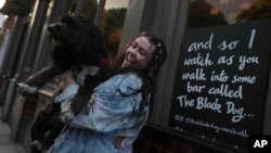 Brodie MacArthur, fan de Taylor Swift, del este de Londres, posa con el perro de un amigo junto a un cartel con letras de Taylor Swift afuera del pub Black Dog en Vauxhall, Londres, el sábado 4 de mayo de 2024.