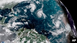 This enhanced satellite image made available by NOAA shows Tropical Storm Florence, center, in the Atlantic Ocean on Saturday, Sept. 8, 2018.