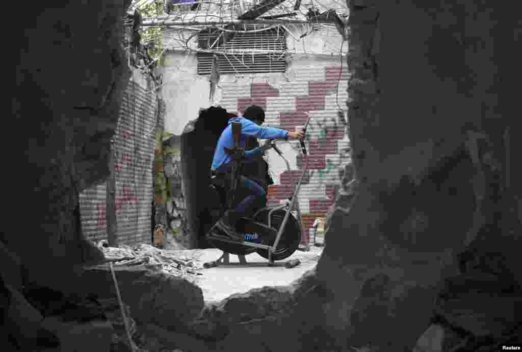 Seorang pemberontak Suriah melakukan latihan fisik seperti terlihat dari lobang sebuah dinding di distrik Seif El Dawla, kota Aleppo, Suriah.