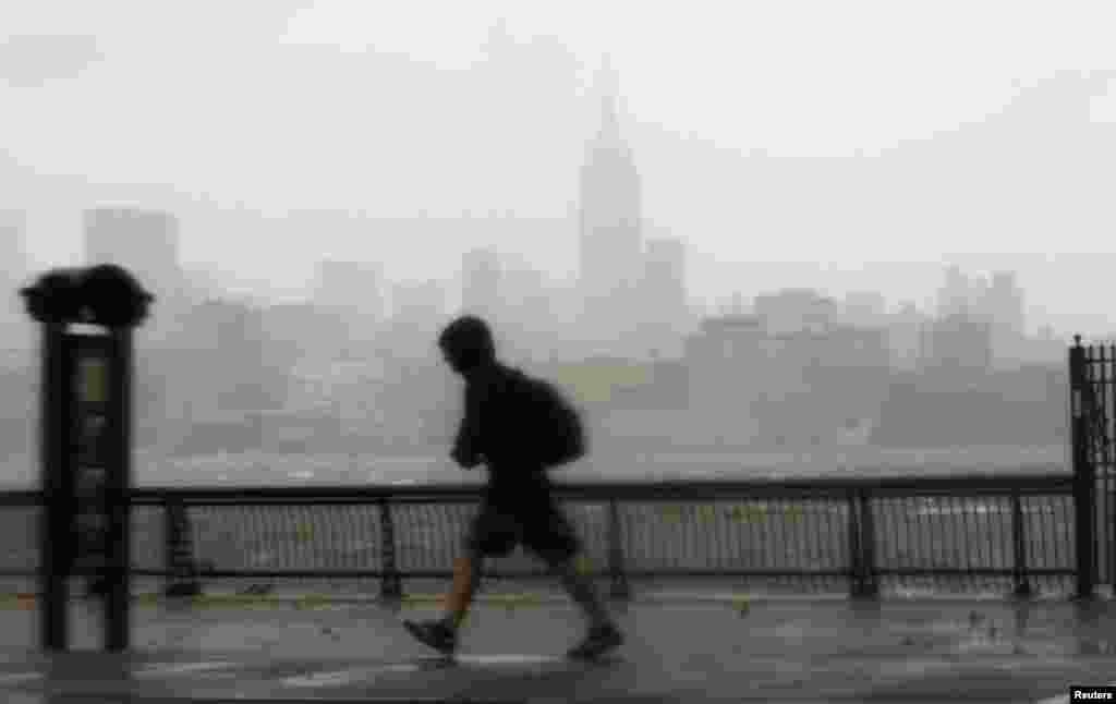 10月29日,一位男士冒着风雨走在新泽西州霍博肯的哈德逊河畔。对岸纽约市摩天大楼依稀可见。