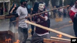 A demonstrator wearing a mask throws a plank of wood into a flaming barricade during a protests in Santiago, Chile, Saturday, Oct. 19, 2019. The protests started on Friday afternoon when high school students flooded subway stations, jumping…