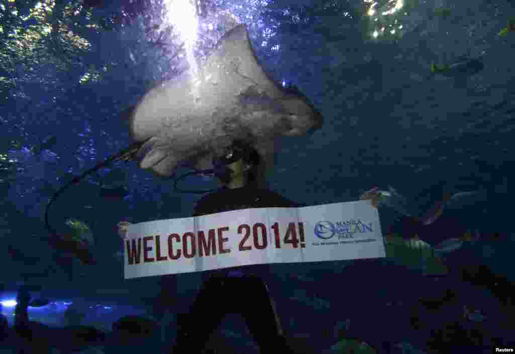 A professional diver holds a "Welcome 2014" banner while swimming next to a stingray during New Year's Eve celebrations inside a large aquarium at an ocean park, Manila, Philippines, Dec. 31, 2013. 