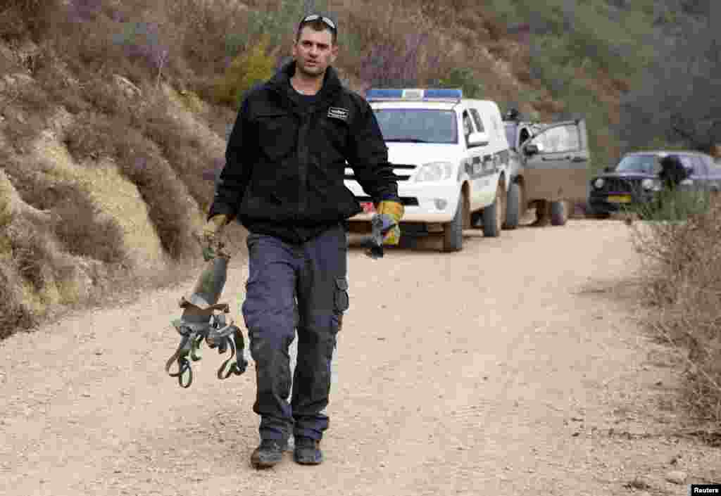 An Israeli police explosive expert carries the remains of a rocket after it landed near the northern town of Kiryat Shmona, Israel, Dec. 29, 2013. 