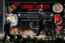 People wearing face masks walk past a sign advertising a restaurant in Mexico City, June 5, 2020.