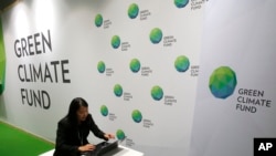 FILE - A woman works her computer at the Green Climate Fund stand at the COP21, United Nations Climate Change Conference, Monday, Nov. 30, 2015 in Le Bourget, north of Paris.