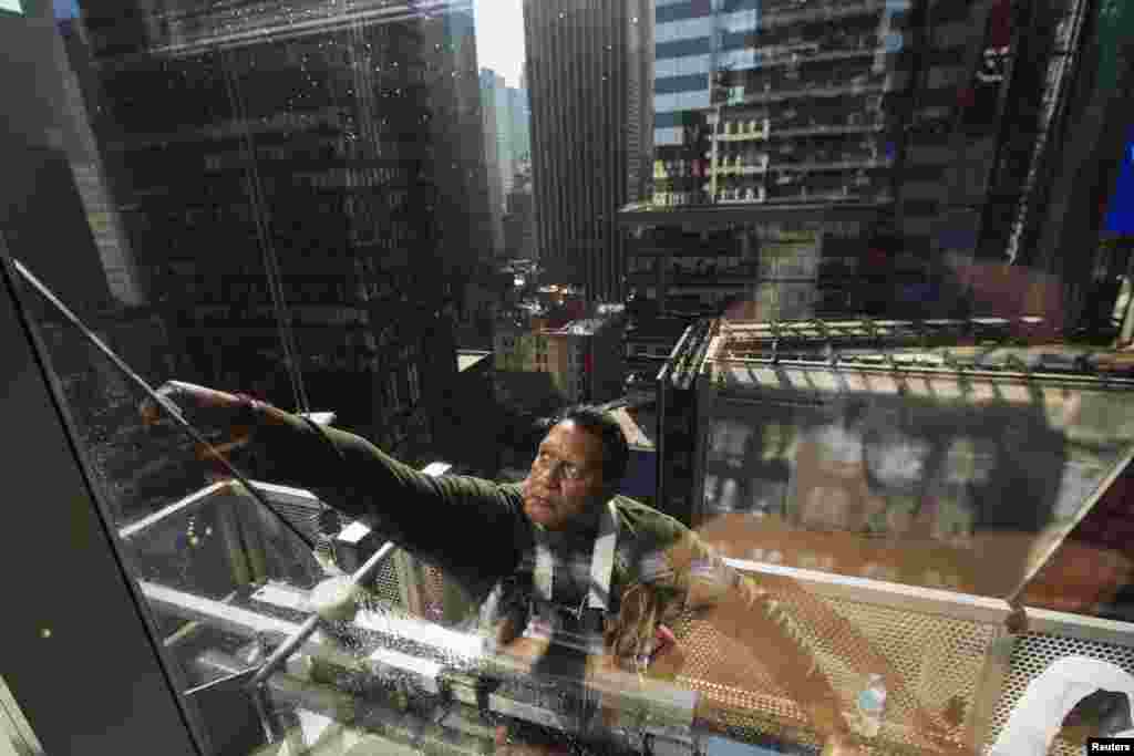 Seorang pembersih jendela dengan menggunakan alat pembersihnya membersihkan jendela-jendela pada hari pertama musim panas di New York Times Square.