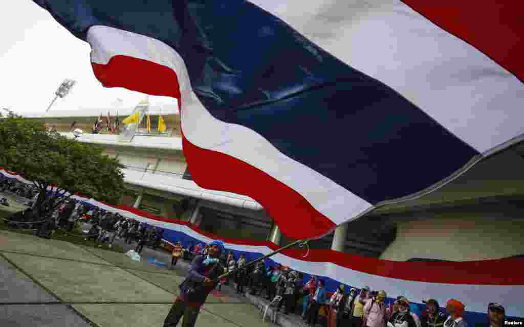An anti-government protester waves a Thai national flag at the gymnasium where candidates register for upcoming elections in Bangkok, Dec. 25, 2013.