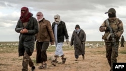 Men suspected of being an Islamic State (IS) group's fighter walk next to a member of the Kurdish-led Syrian Democratic Forces (SDF) as they wait to be searched after leaving the IS group's last holdout of Baghouz, Syria, Feb. 27, 2019.