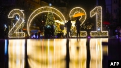 Women walk under an umbrella in front of a 2021 sign displayed in downtown Pristina on December 30, 2020, as Kosovars prepare to celebrate the New Year 2021 at their homes, amid the ongoing Covid-19 (novel coronavirus) pandemic. (Photo by Armend NIMANI / 