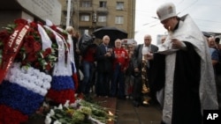 A Russian Orthodox priest prays as Moscovites light candles at a memorial to three men killed in the August 1991 hard line Communist coup attempt during a ceremony marking the 20th anniversary of the failure of the coup in downtown Moscow, Saturday, Aug.
