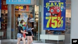 FILE - Two girls walk past a store with sale signs displayed at Great Lakes Mall, June 10, 2020, in Mentor, Ohio. Sales for retailers have plunged since the coronavirus pandemic. 