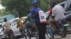 A stream of boda bodas passes a woman holding a poster advertising the launch of a new VOA frequency in Juba in March 2013.