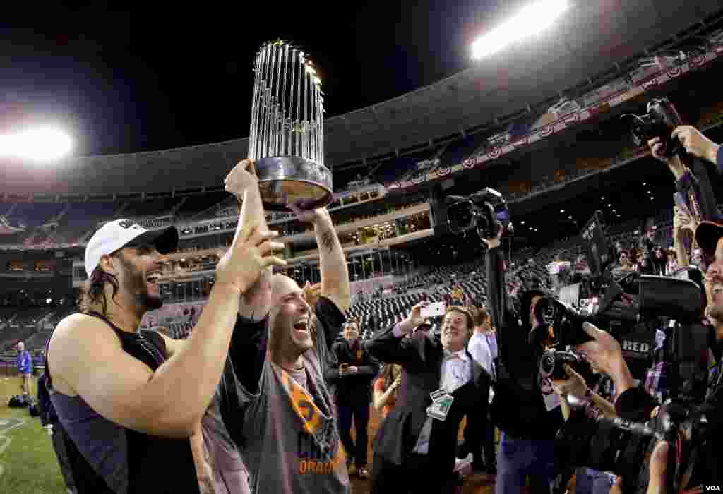 San Francisco Giants left fielder Michael Morse (left) and starting pitcher Tim Hudson hold up the trophy after their 3-2 win in Game 7 of baseball's World Series against the Kansas City Royals, Kansas City, Missouri, Oct. 29, 2014.
