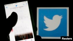 FILE - A man reads tweets on his phone in front of a displayed Twitter logo.