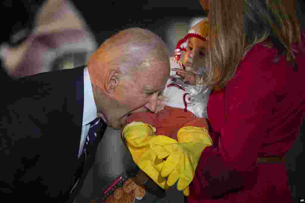 President Joe Biden jokingly bites the leg of a baby, as he and first lady Jill Biden host a trick-or-treating event, at the South Lawn of the White House in Washington, Oct. 30, 2024.