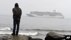 FILE - A man stands on the Bering Sea shore looking at the luxury cruise ship Crystal Serenity anchored just outside Nome, Alaska, Aug. 21, 2016.