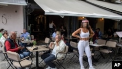 A cafe-restaurant employee stands outside as people drink coffee in Monastiraki district of Athens, May 25, 2020, as Greece restarted regular ferry services to its islands, and cafes and restaurants were also back open for business.
