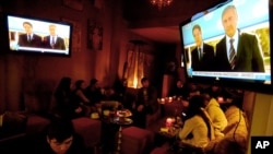 People sit at a coffee bar as TV screens show Greek Cypriot President Nicos Anastasiades, left, and the leader of the Turkish Cypriots, Mustafa Akinci, delivering holiday wishes together in Nicosia, Dec. 24, 2015.