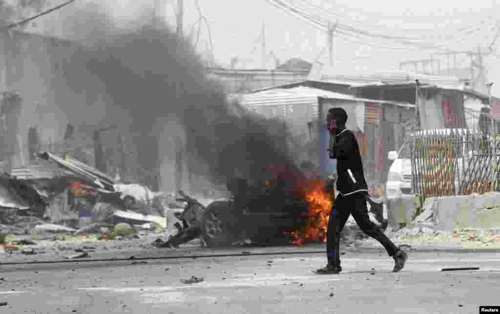 A man talks on his mobile phone as he walks at the scene of an explosion near the entrance of the airport in Somalia's capital Mogadishu, Feb. 13, 2014.