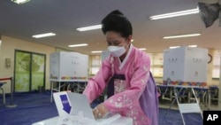 一位戴上口罩避免新冠病毒傳播的女士在南​韓首爾的投票所投下國會選舉票 。(2020年4月15日)