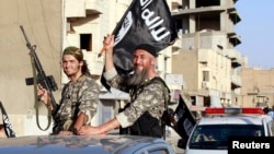 FILE - Fighters with the militant group Islamic State wave flags as they take part in a military parade along the streets of Raqqa province, northern Syria. 