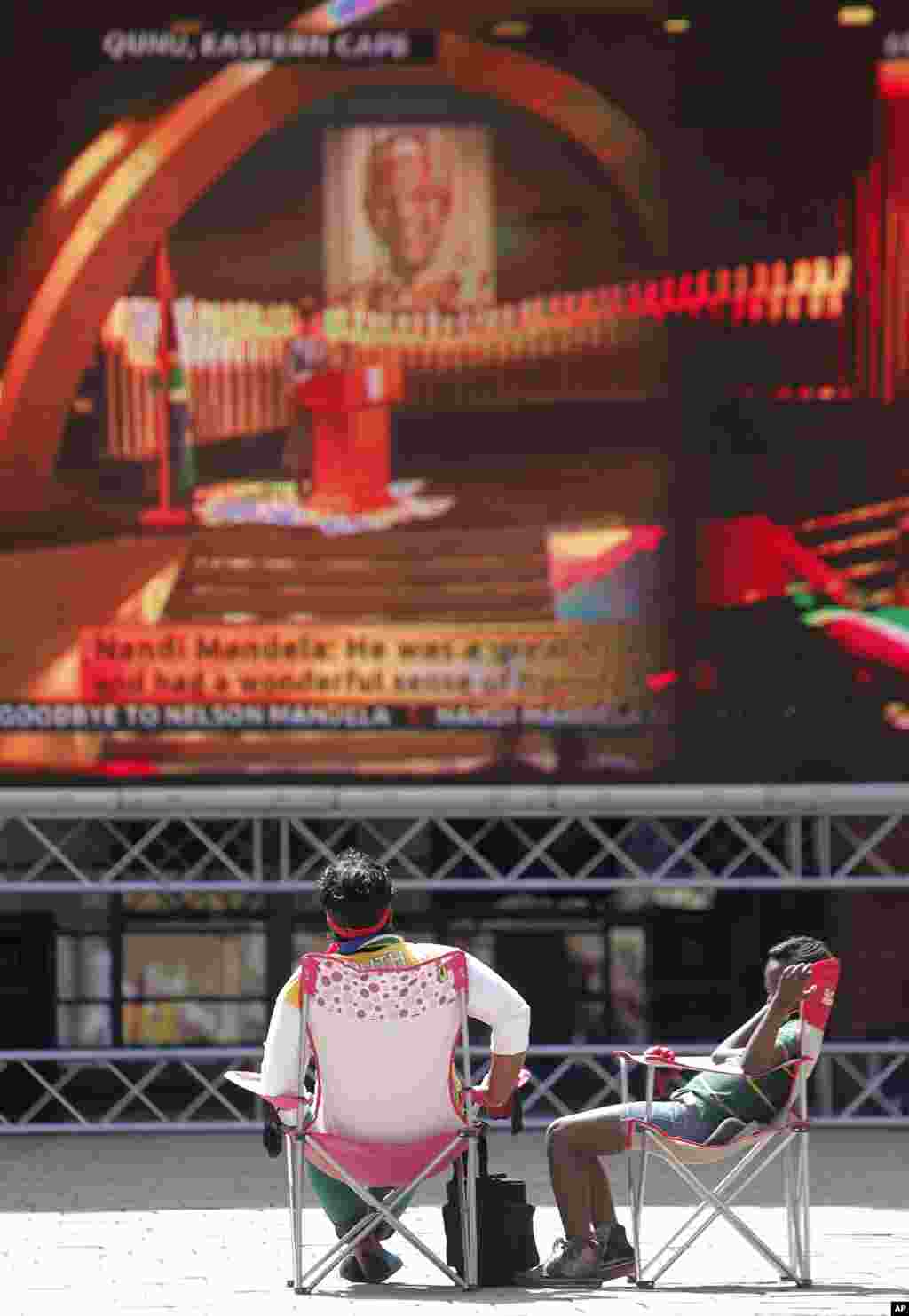 Two people follow the proceedings of Nelson Mandela's funeral on a big screen in Nelson Mandela square in Sandton, Johannesburg.