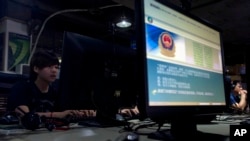 FILE - Computer users sit near a monitor with a message from the Chinese police on the proper use of the Internet at an Internet cafe in Beijing, China, August 19, 2013.