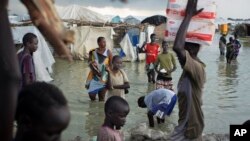 Displaced South Sudanese walk through flood waters in a camp for the displaced at the United Nations Mission in South Sudan (UNMISS) base in the town of Bentiu, South Sudan Monday, Sept. 22, 2014. (AP Photo/Matthew Abbott)
