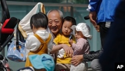 Seorang pria lansia bermain dengan anak-anak di dekat gedung perniagaan di Beijing, 10 Mei 2021. (Foto: Andy Wong/AP Photo)