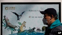 FILE - A man wearing a protective face mask walks by a propaganda poster promoting to protect wildlife after authorities crackdowns on wild animal markets following the coronavirus outbreak in Beijing, March 11, 2020. 