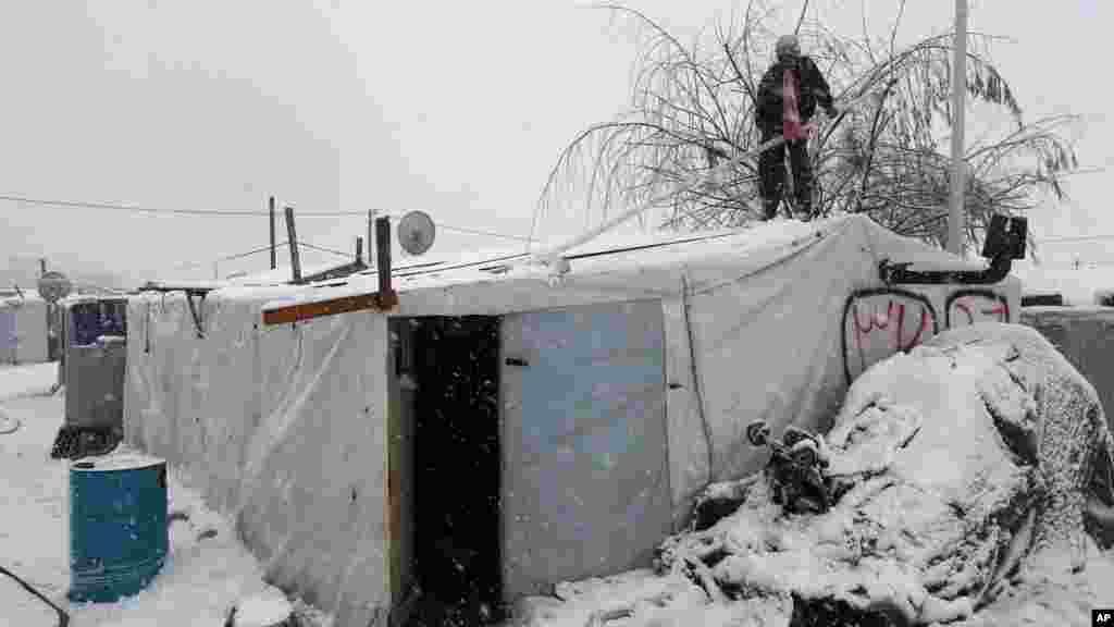 A Syrian man stands on top of his tent as he removes snow at a refugee camp in Deir Zannoun village, in the Bekaa valley, east Lebanon, Jan. 7, 2015.