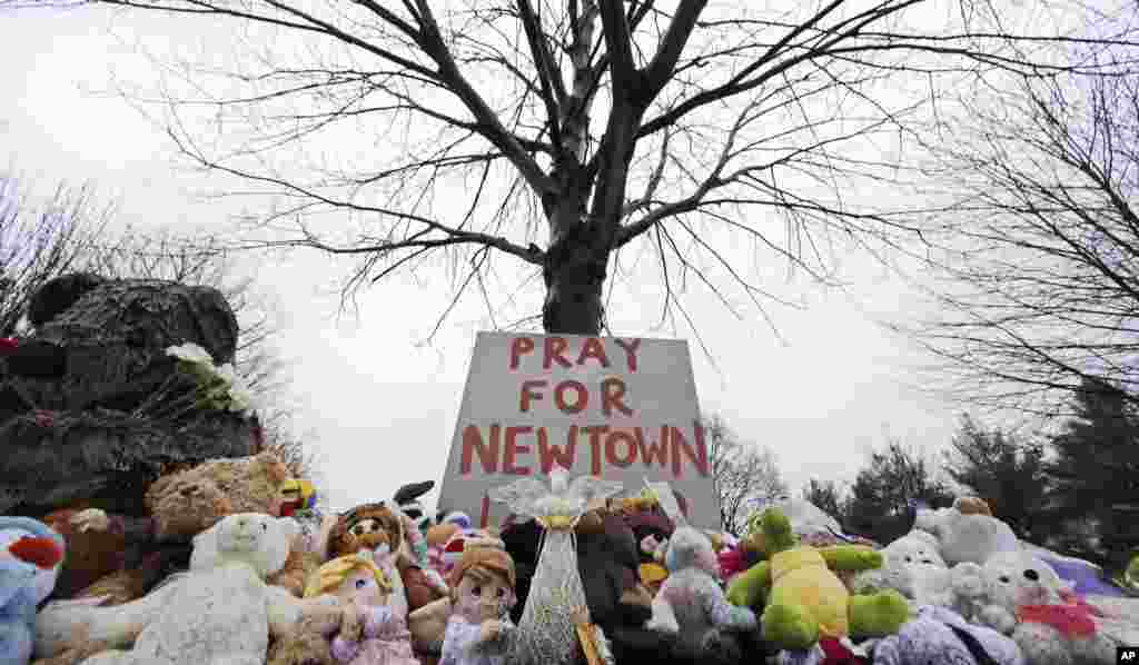 Stuffed animals and a sign calling for prayer rest at the base of a tree near the Newtown Village Cemetery in Newtown, Conn., Dec. 17, 2012.
