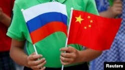 一名中国男孩在北京人大会堂外手持中俄两国国旗欢迎到访的俄罗斯总统普京。（2016年6月25日）