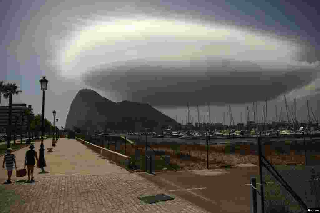 Dua orang berjalan dan di kejauhan tampak Rock of Gibraltar, batu kapur besar yang merupakan wilayah Inggris, dekat perbatasan La Linea de la Concepcion, Spanyol Selatan.