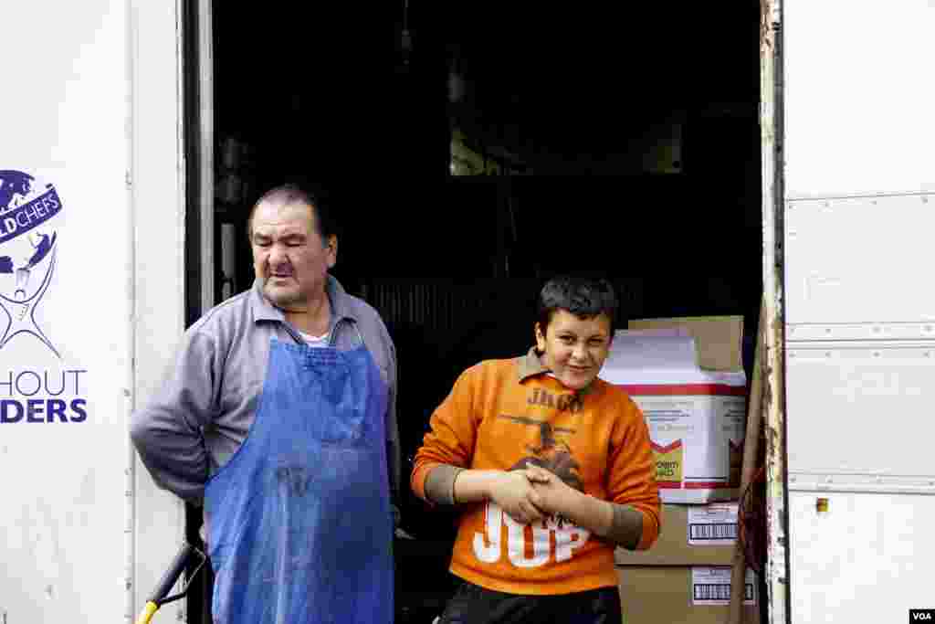 A Greek father and son waiting to hand out food to Idomeni refugees. (Jamie Dettmer for VOA)